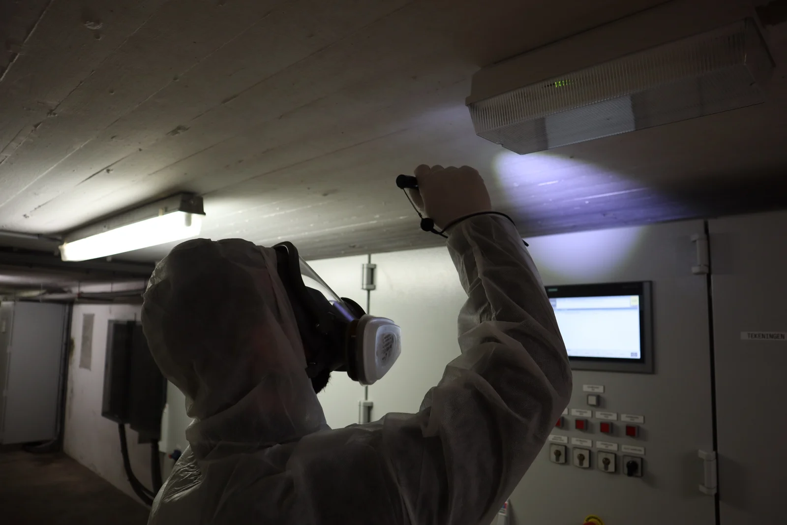 Q-Works bekijkt een plafondaansluiting in een technische ruimte met een zaklamp